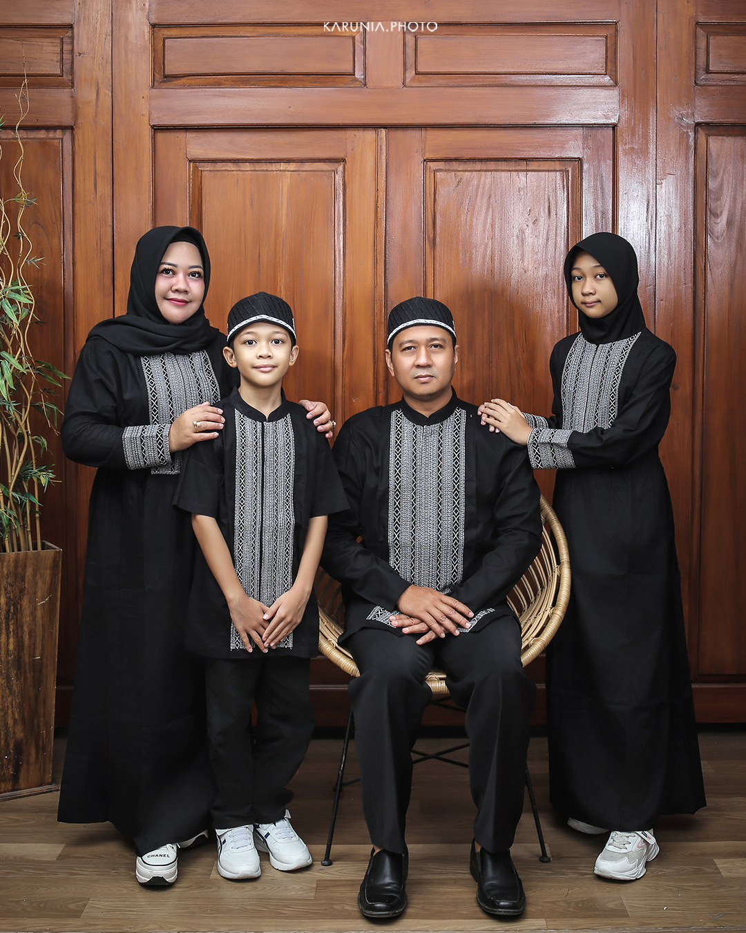 Three siblings sitting on wooden steps in coordinating outfits with genuine smiles and relaxed poses